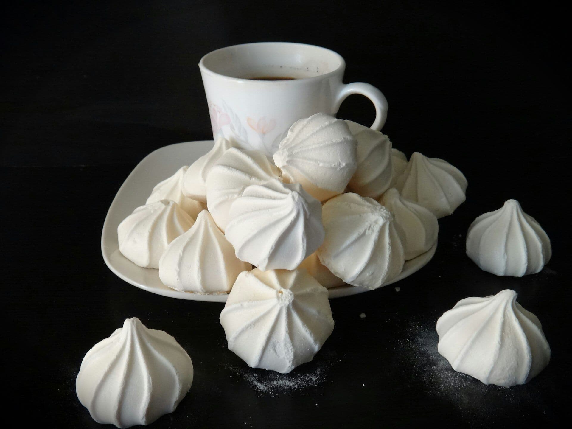 White piped meringues heaped on a plate beside a cup of coffee
