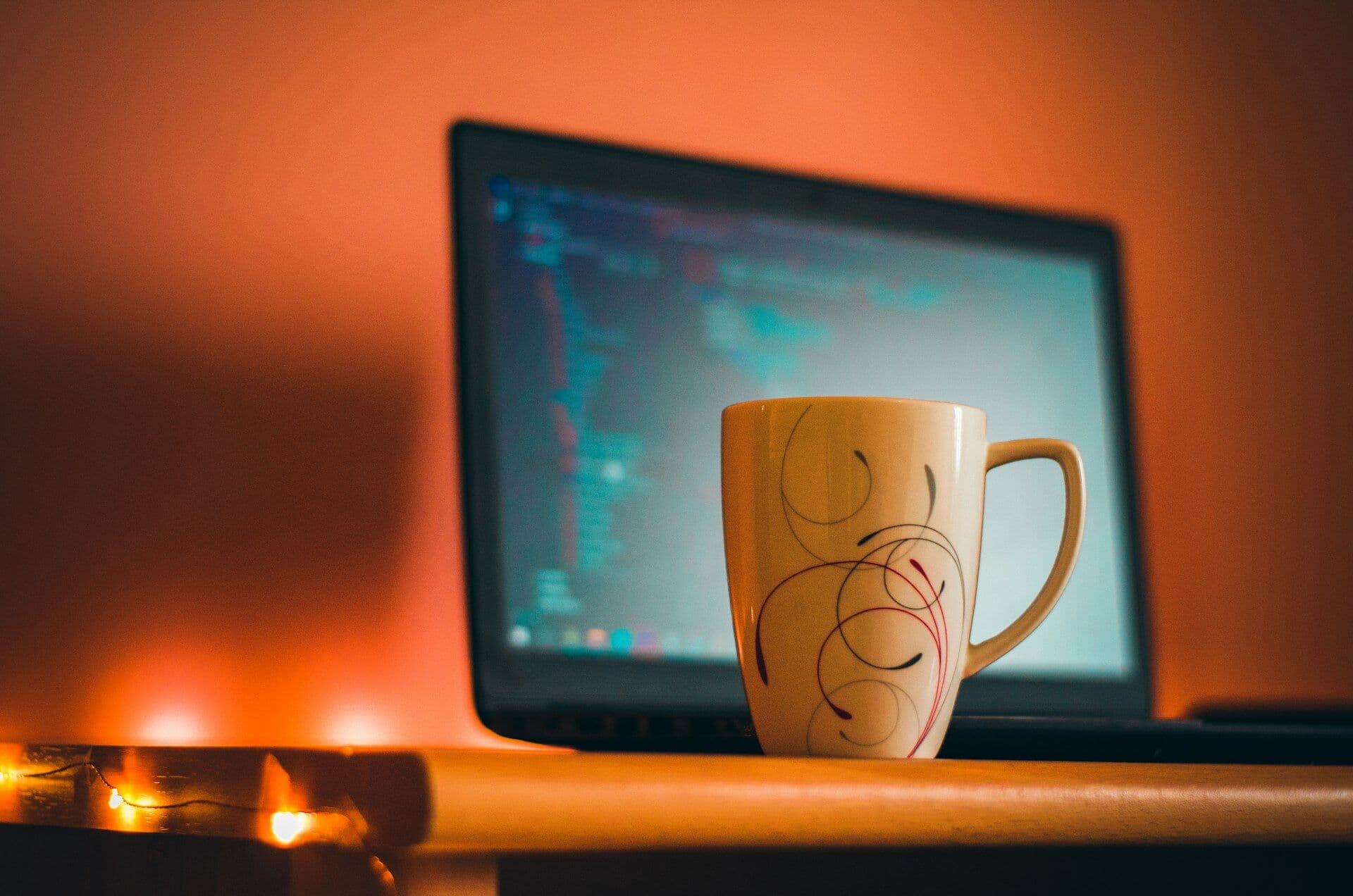 A laptop showing code beside a coffee mug against a warm orange wall